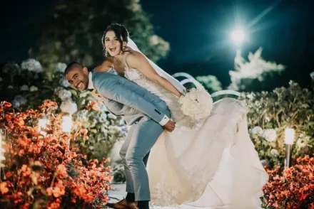 Novio cargando a la novia en un jardín iluminado de noche