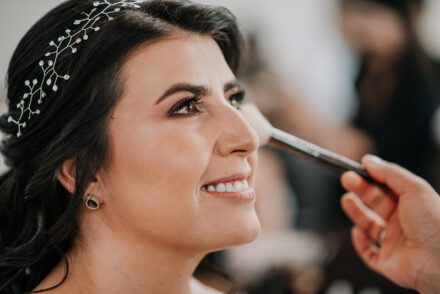 Novia sonriendo mientras la maquillan para su boda.