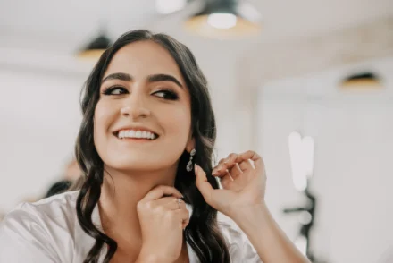 Mujer sonriente colocándose los aretes en la preparación de su boda.