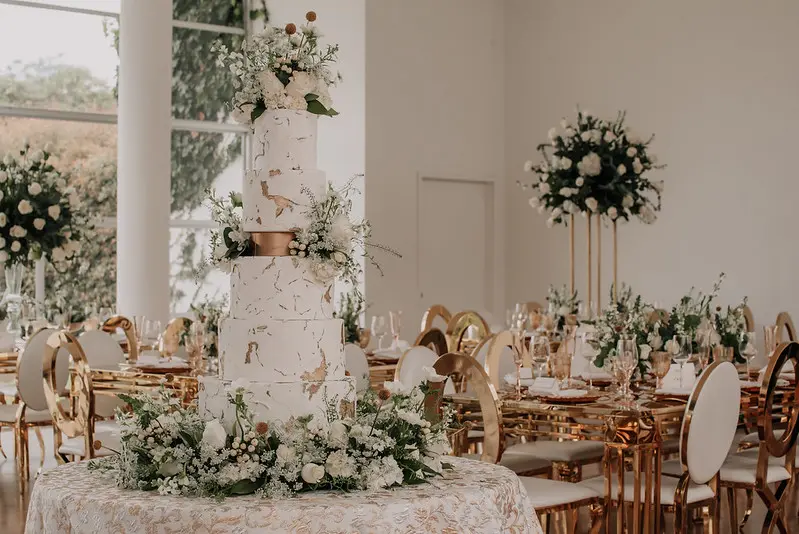 Pastel de boda blanco de varios pisos decorado con cascada de flores blancas en salón