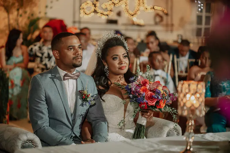 novio con traje azul claro y novia con ramo de flores sentados en la mesa principal durante su recepción de bodas