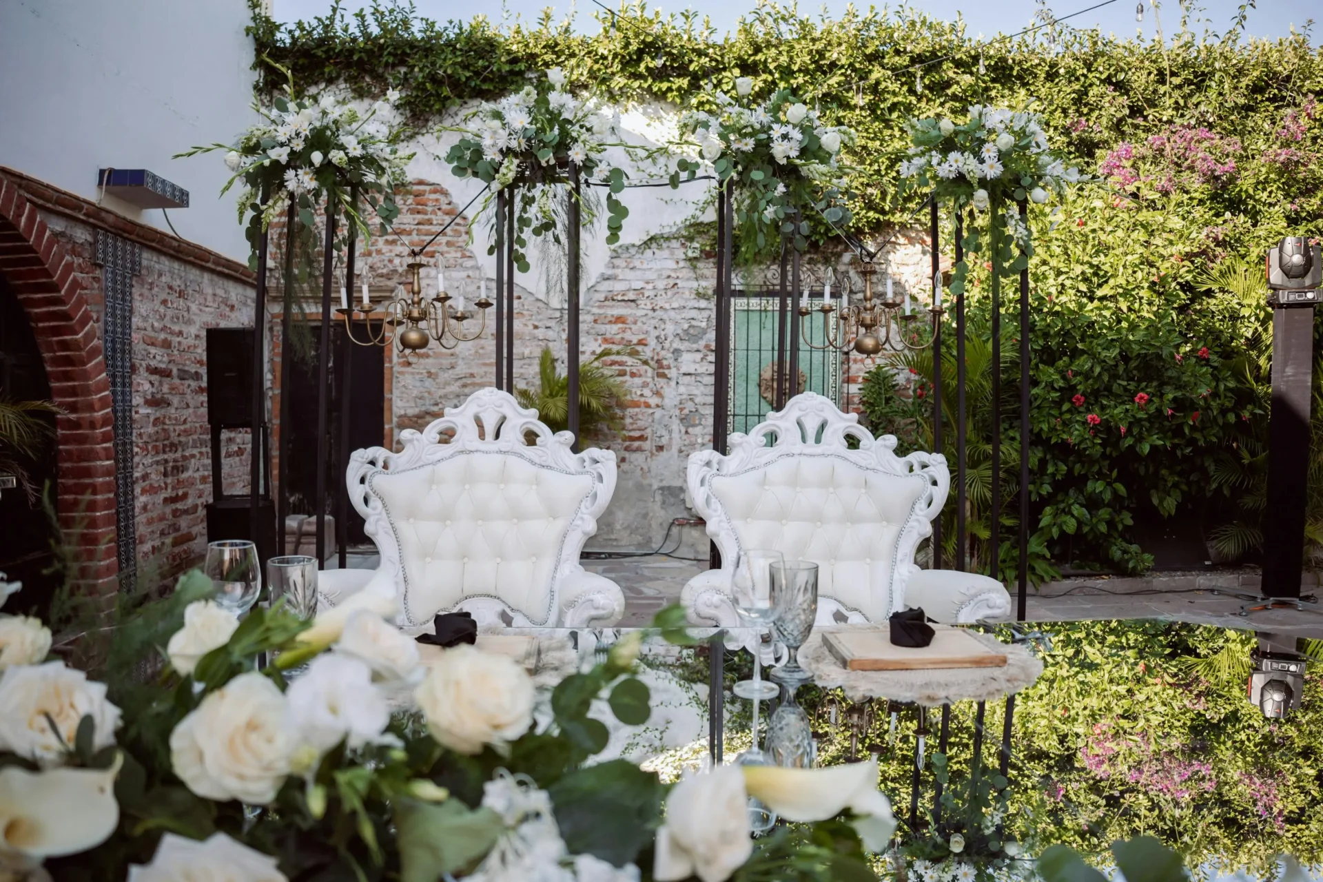 Dos sillas blancas ornamentadas, estilo trono, decoradas con flores blancas y vegetación para una celebración de aniversario al aire libre.