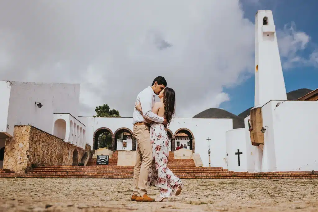 propuesta de matrimonio al aire libre frente a una histórica iglesia blanca, donde el novio besa a su prometida