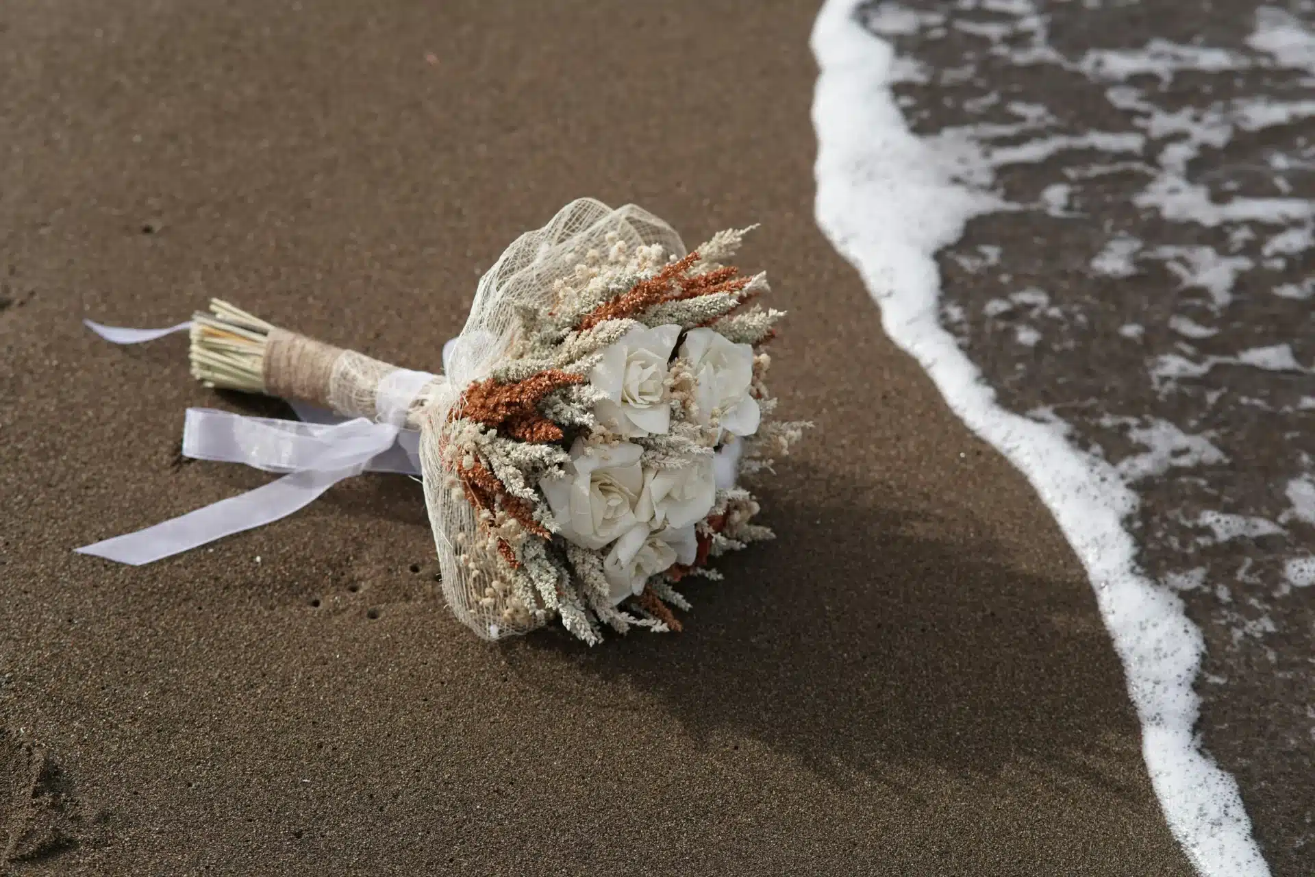Matrimonio en la playa con ramo de novia sobre la arena y olas del mar en una boda romántica