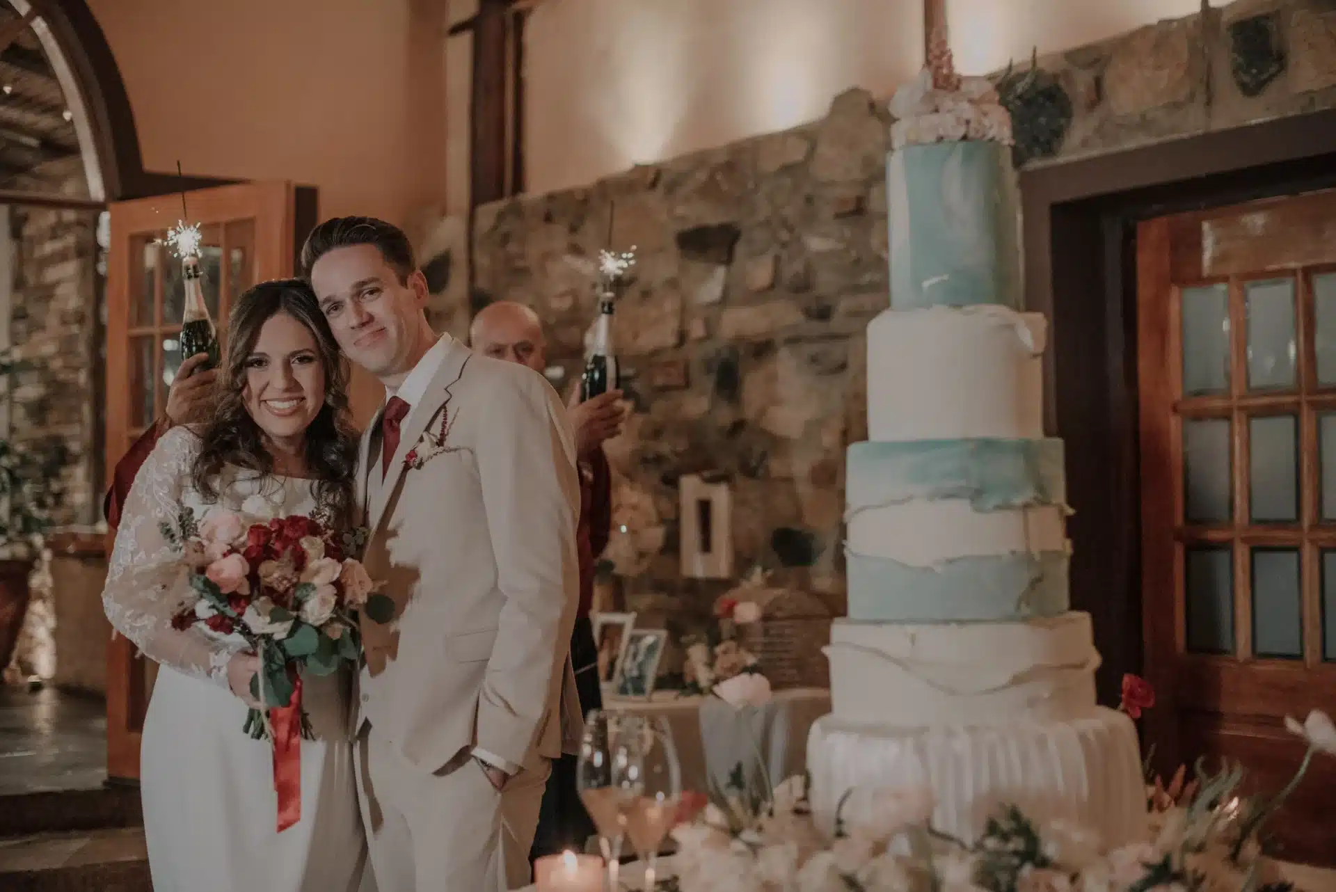 Pareja de recién casados junto a una torta de matrimonio de varios pisos en una boda campestre con estilo elegante. 